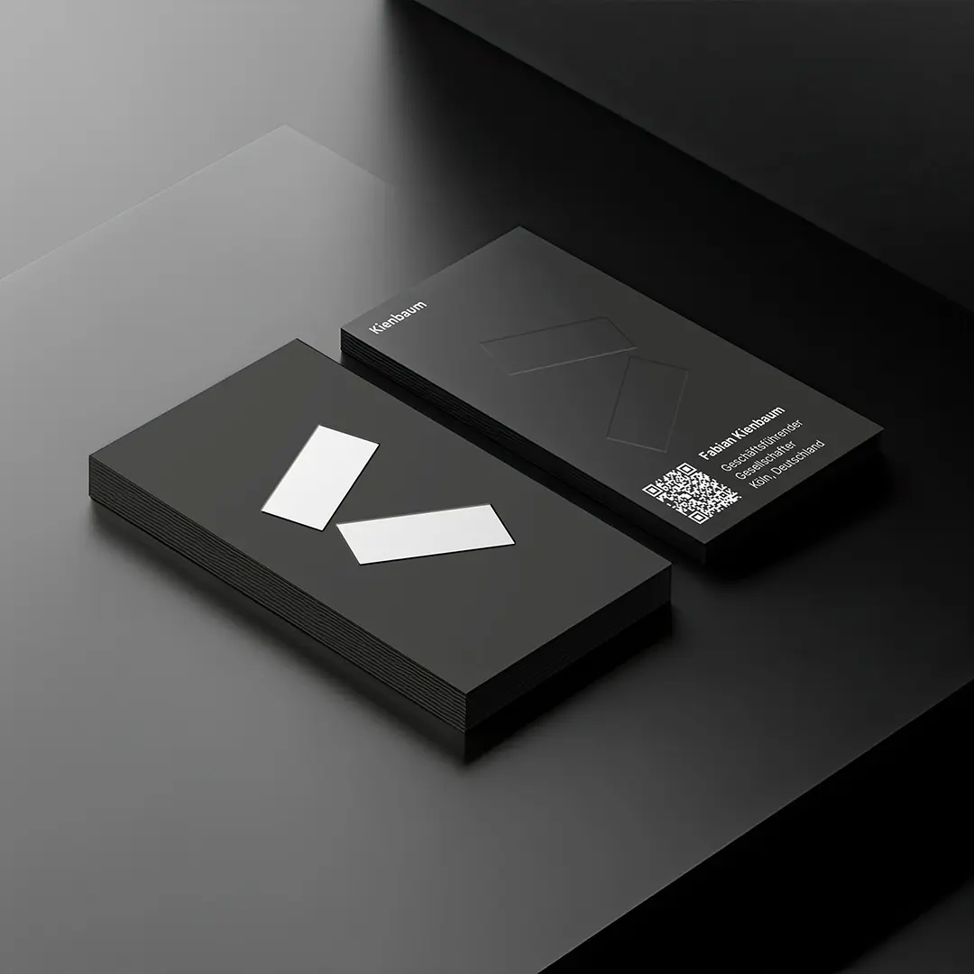 Two stacks of black business cards on a black surface, one showing a minimalist design with two white rectangles, the other showing text, a QR code, and embossed rectangles.