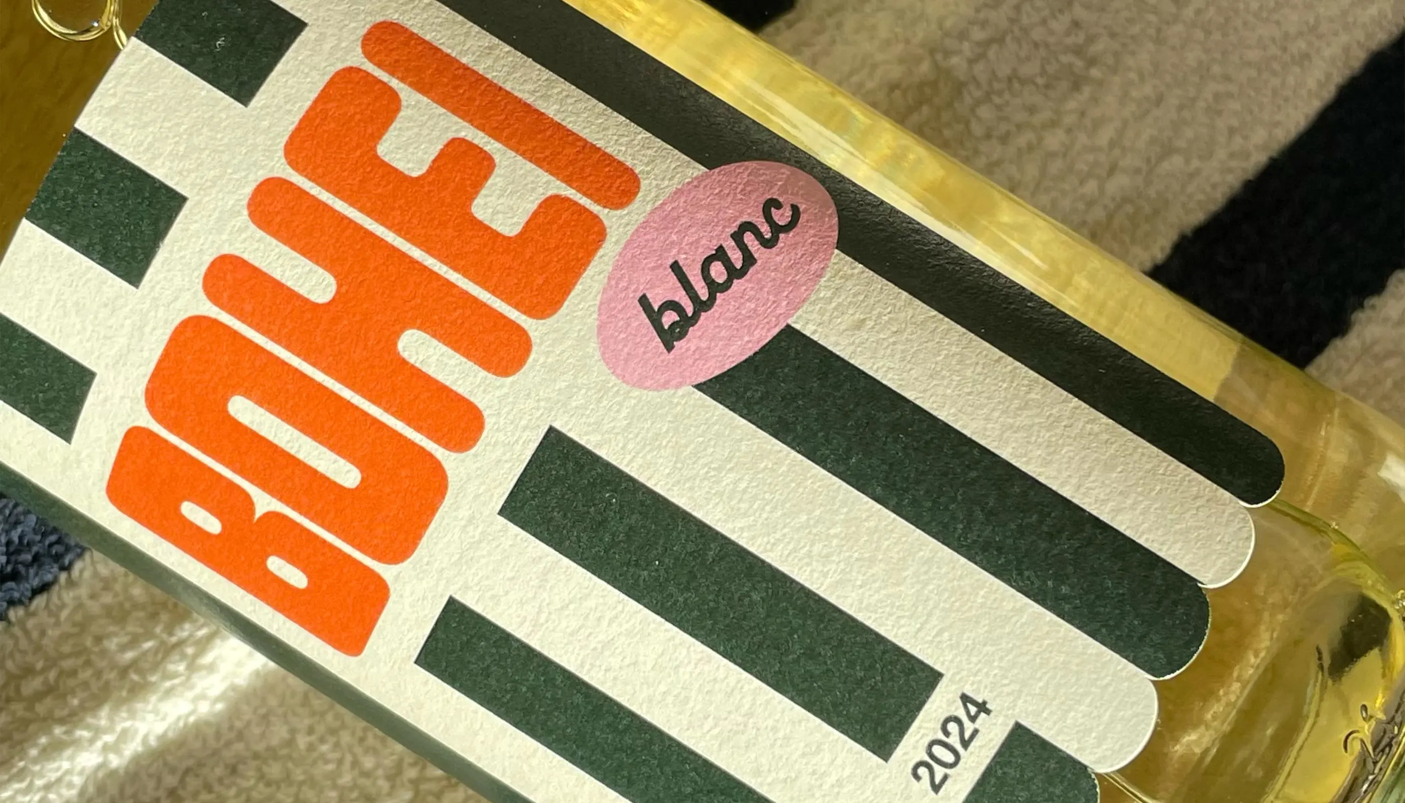 Close-up of a white wine bottle label with bold orange text 'BOHE', pink oval with 'blanc', black vertical stripes, and the year 2024.