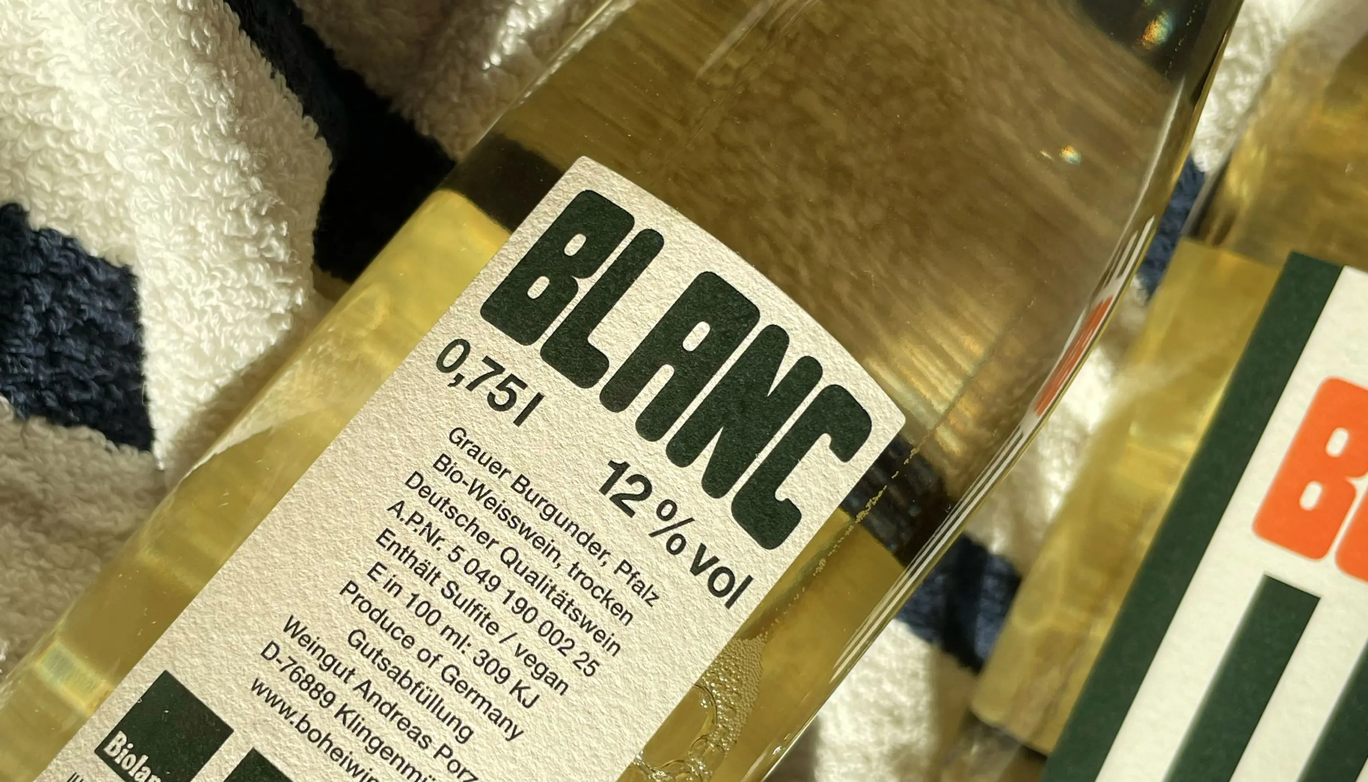 Close-up of a white wine bottle label showing 'BLANC' with 12% alcohol, 0.75l, and German text about the wine.